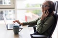 Cheerful young beautiful woman in glasses talking on mobile phone and using laptop with smile while sitting at her working place Royalty Free Stock Photo