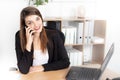 Cheerful young beautiful woman talking on phone using laptop with smile while sitting at office working place Royalty Free Stock Photo