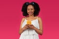 Cheerful young black curly woman typing on phone, chatting in social networks