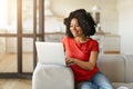 Cheerful young black woman using laptop while sitting on sofa at home Royalty Free Stock Photo