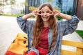 Cheerful young blonde hipster woman student with backpack looking to camera with happy face. Peace gesture.