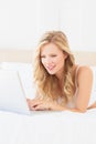 Cheerful young blonde lying on her bed using laptop Royalty Free Stock Photo