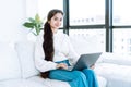 Cheerful young brunette saleswoman manager holding laptop looking at camera and sitting on white couch Royalty Free Stock Photo