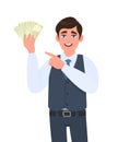 Cheerful young business man in waistcoat showing cash or currency notes and pointing finger. Trendy person holding banknotes.