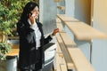 Cheerful young business woman standing in modern office talking on her mobile phone. Beautiful female model using cell phone Royalty Free Stock Photo