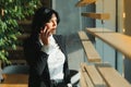 Cheerful young business woman standing in modern office talking on her mobile phone. Beautiful female model using cell phone Royalty Free Stock Photo