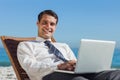 Cheerful young businessman lying on a deck chair with his computer Royalty Free Stock Photo