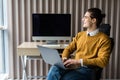 Cheerful young businessman sitting on chair with laptop on legs in office