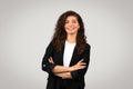 Cheerful young businesswoman in black blazer standing with folded arms and smiling against light grey background Royalty Free Stock Photo