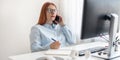 Cheerful young businesswoman sitting at her workplace, talk on mobile cell phone use a laptop computer in the office Royalty Free Stock Photo