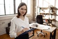 Cheerful young businesswoman stand in room and look on camera. She hold plastic folder with document and write.