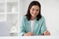Cheerful young caucasian businesswoman in suit makes notes at table with laptop in office interior Royalty Free Stock Photo