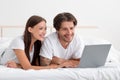 Cheerful young caucasian couple lie on bed with laptop have video call, watch video, chatting, searching Royalty Free Stock Photo