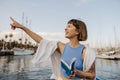 Cheerful young caucasian lady points her finger to sky, standing near sea on warm summer day. Royalty Free Stock Photo