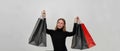 Cheerful young caucasian woman wearing black clothes smiling away, posing with arms raised holding shopping bags Royalty Free Stock Photo