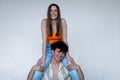 Cheerful young couple in bright summer clothes, gray studio background, copy space. Smiling girl sitting on shoulders of Royalty Free Stock Photo