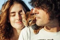 Cheerful young couple having fun on the beach with their bengal cat