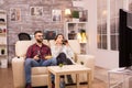 Cheerful young couple sitting on sofa and watching a movie on tv Royalty Free Stock Photo