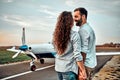 Cheerful young couple standing and hugging near private airplane