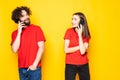 Cheerful young couple talking on mobile phones over yellow background Royalty Free Stock Photo