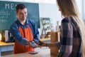 Cheerful young Down Syndrome waiter taking contactless smartphone payment from costumer in take away restaurant. Royalty Free Stock Photo