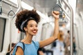 Cheerful young ethnic woman standing and holding handle while riding in subway train