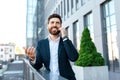 Cheerful young european businessman with beard in suit calling by phone on balcony of modern office building Royalty Free Stock Photo