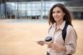 Cheerful young european female student in casual and headphones with backpack and smartphone go to study