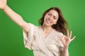 Cheerful young european lady take selfie, ok sign, isolated on green studio background
