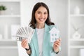 Cheerful young european woman in suit shows house and lot of money in office interior