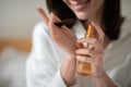 Cheerful young european woman on white bed applies spray on hair in bedroom interior, close up, cropped