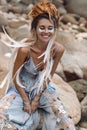 Cheerful young fashionable woman sitting on the stone beach Royalty Free Stock Photo