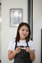 A young female entrepreneur wearing black apron standing in her own modern coffee shop.