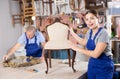 Cheerful young female furniture restorer showing his vintage furniture workshop