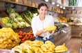 Cheerful young female shopper selecting ripe bananas in store Royalty Free Stock Photo