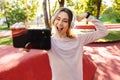 Cheerful young fitness sports woman posing outdoors in park listening music with earphones take selfie by mobile phone Royalty Free Stock Photo