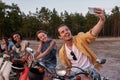 Cheerful young friends, motorcycle riders smiling while taking a selfie together, sitting on scooters outside the city