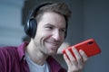 Cheerful young german man in wireless headphones holding smartphone in hand, recording audio message