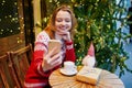 Cheerful young girl in holiday sweater in cafe decorated for Christmas