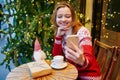 Cheerful young girl in holiday sweater talking with someone on video chat on Christmas