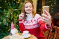 Cheerful young girl in holiday sweater talking with someone on video chat on Christmas
