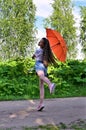 cheerful young girl with orange umbrella is having fun on sunny summer day outdoors against background of green foliage, Royalty Free Stock Photo