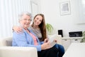 Cheerful young girl sharing time with an old senior woman and teaching internet with a computer tablet Royalty Free Stock Photo