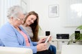 Cheerful young girl sharing time with an old senior woman and teaching internet with a computer tablet Royalty Free Stock Photo