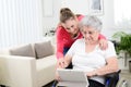 Cheerful young girl teaching internet with computer tablet and sharing time with an old senior woman on wheelchair