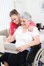 Cheerful young girl teaching internet with computer tablet and sharing time with an old senior woman on wheelchair