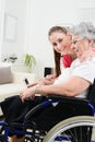 Cheerful young girl teaching internet with computer tablet and sharing time with an old senior woman on wheelchair Royalty Free Stock Photo