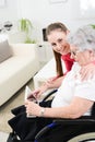 Cheerful young girl teaching internet with computer tablet and sharing time with an old senior woman on wheelchair Royalty Free Stock Photo