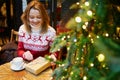 Girl in holiday sweater drinking coffee or hot chocolate in cafe decorated for Christmas Royalty Free Stock Photo