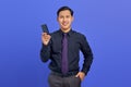 Cheerful young handsome businessman holding smartphone and looking at camera on purple background Royalty Free Stock Photo